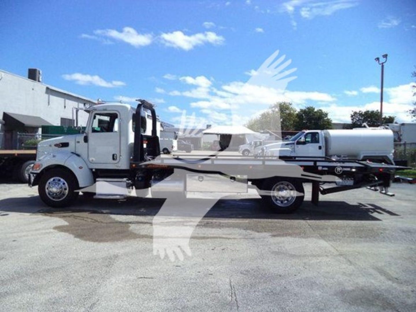 Peterbilt 337 rollback tow truck shown in side profile with a long flatbed and a white cab, chrome wheels, and a tanker trailer in the background.