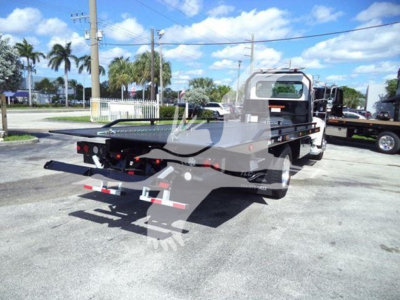 Image of a tow truck (Peterbilt 337 style) rear/side view with a flatbed rollback body. Visible text includes no legible labels on parts from distance. Overall vehicle appears in-service.