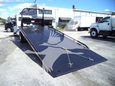 Peterbilt 337 rollback tow truck image showing lengthy black flatbed with ramps and chains, cab in background, used vehicle.