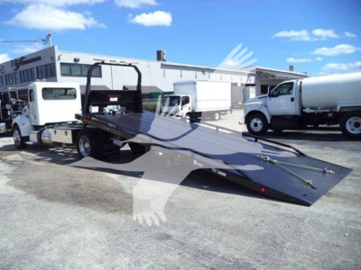 Peterbilt 337 rollback tow truck with flatbed in lowered position; white cab with loading deck and other trucks in background.