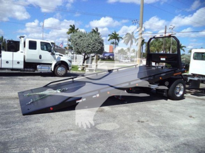 Peterbilt 337 rollback tow truck with flatbed trailer and other trucks in background.