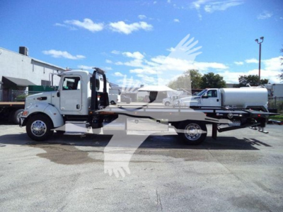 Peterbilt 337 rollback tow truck shown in side profile with a long flatbed and a white cab, chrome wheels, and a tanker trailer in the background.