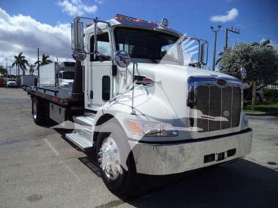 Peterbilt 337 tow truck/rollback with white cab showing chrome grille and mirrors, flatbed at rear, side steps, Peterbilt emblem, daytime.