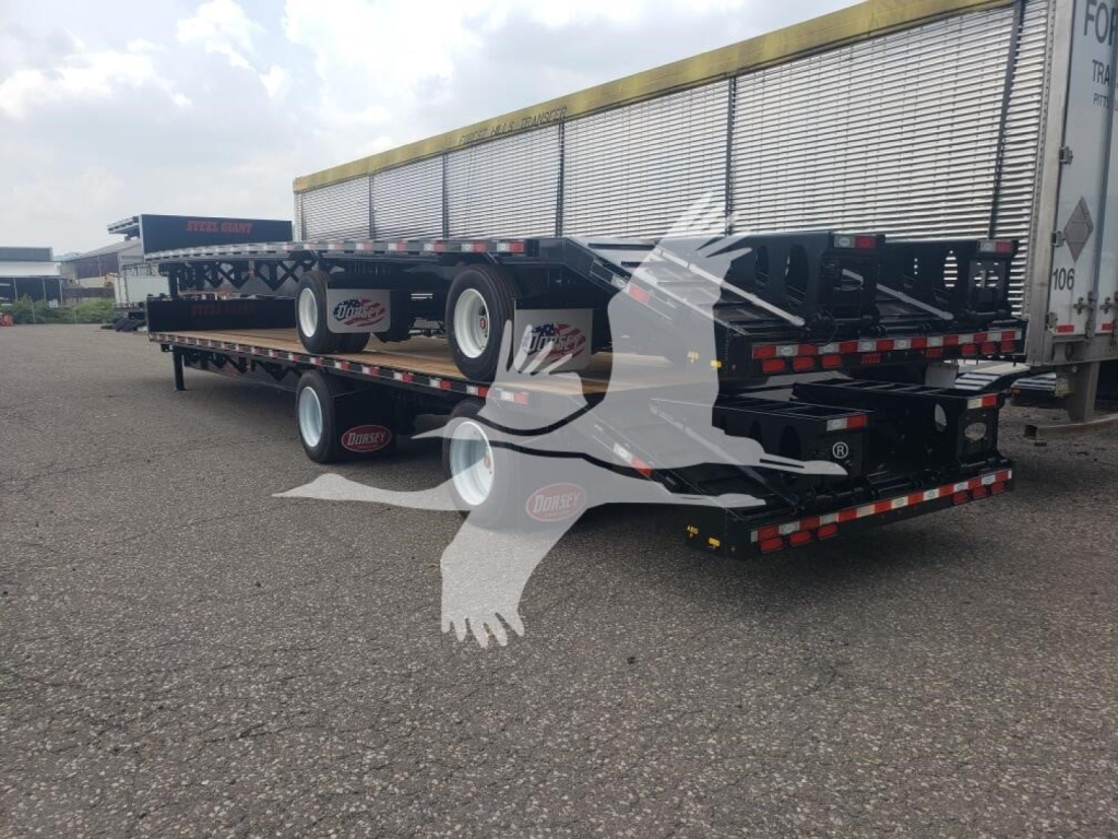 Trailer deck with beavertail trailer in a parking lot, rear view showing multiple axles and flatbed sections.