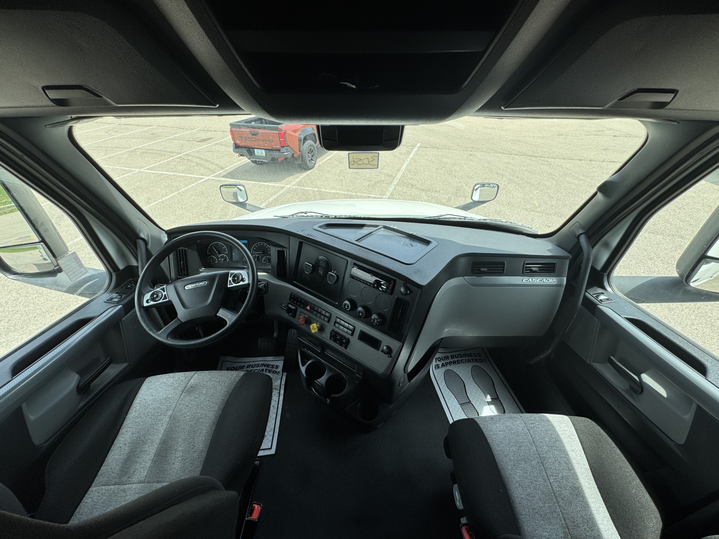 Freightliner Cascadia 126 cab interior showing steering wheel and dashboard with gauges and center controls.