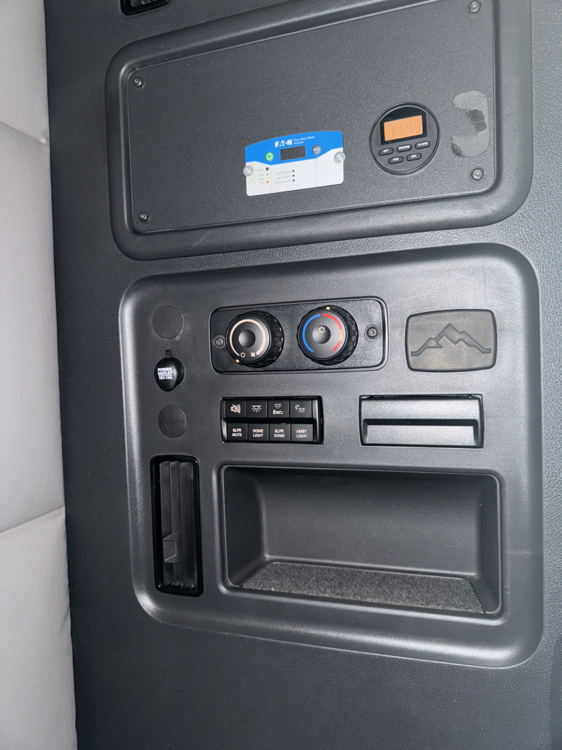 Dashboard area of a 2021 Freightliner Cascadia showing control gauges and a small digital display, with a blue card sticker and a circular device on the panel.