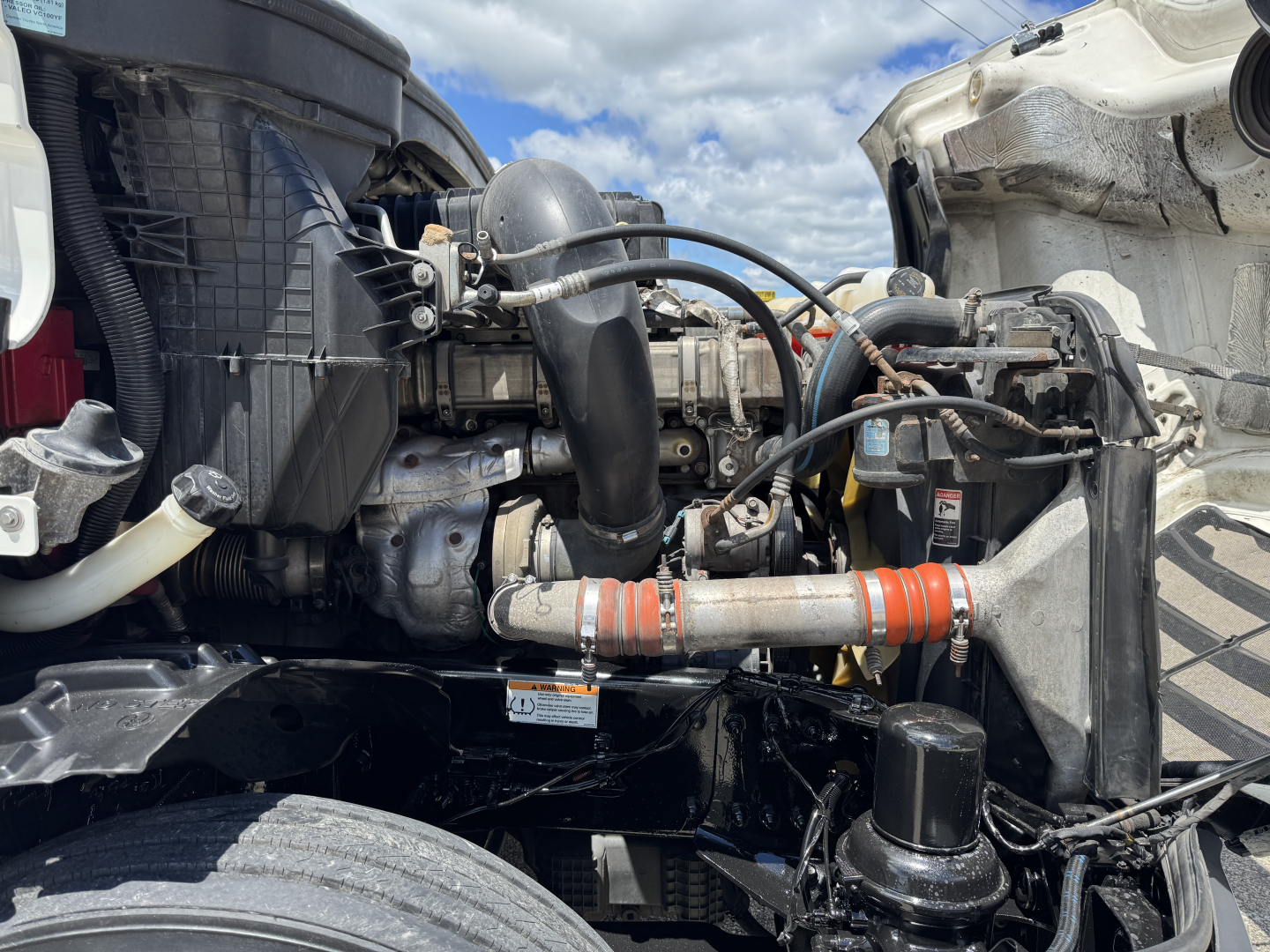 Freightliner Cascadia 126 engine bay showing hoses, radiator, and engine components with orange hoses in view.