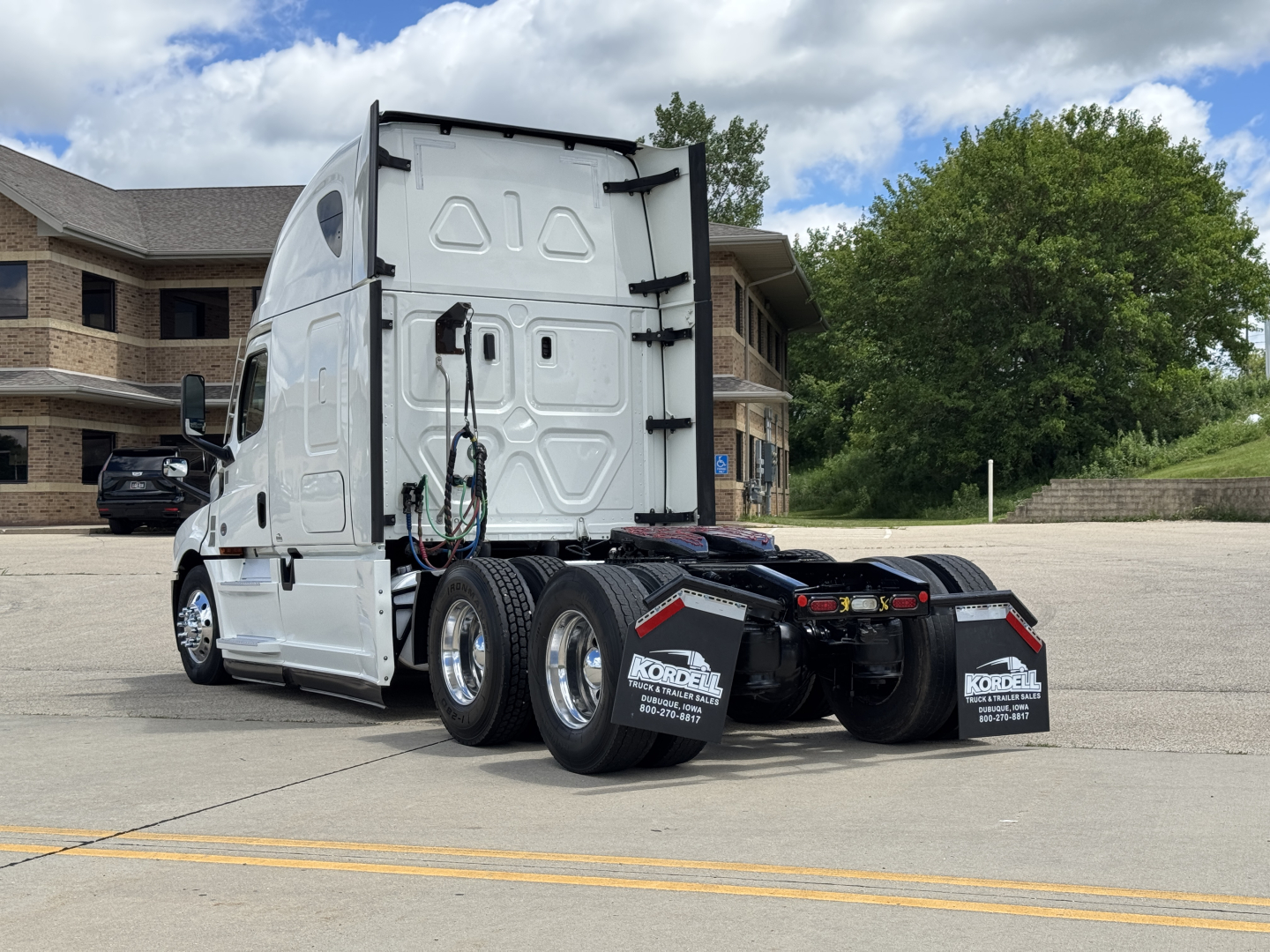 Freightliner Cascadia 126 tractor rear view showing dual rear axles and fifth wheel, white exterior, glossy mirrors, back of sleeper cab.