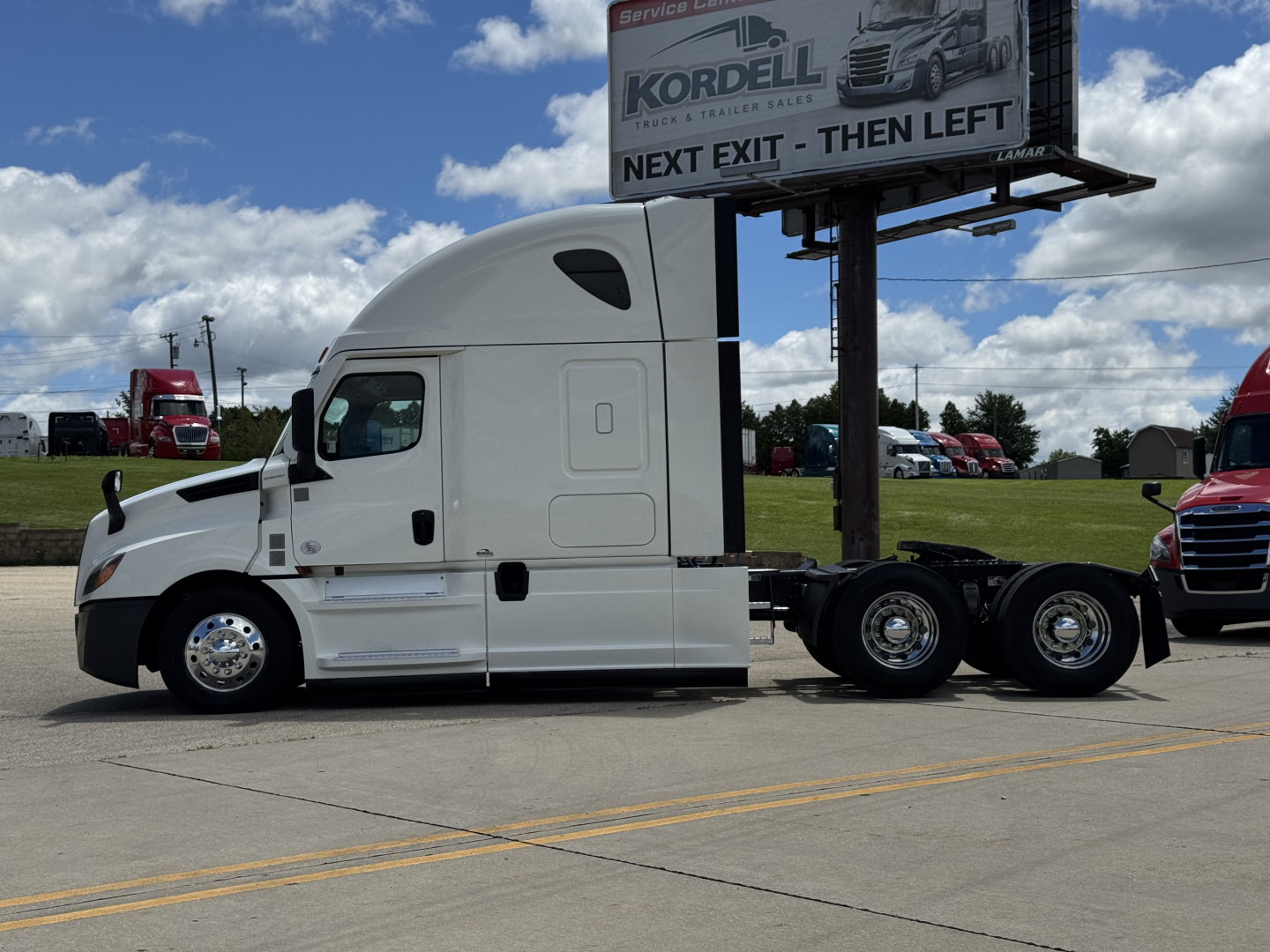 Tractor-trailer in a dealership lot with white Freightliner Cascadia 126 sleeper cab, side view showing chassis and dual rear axles.