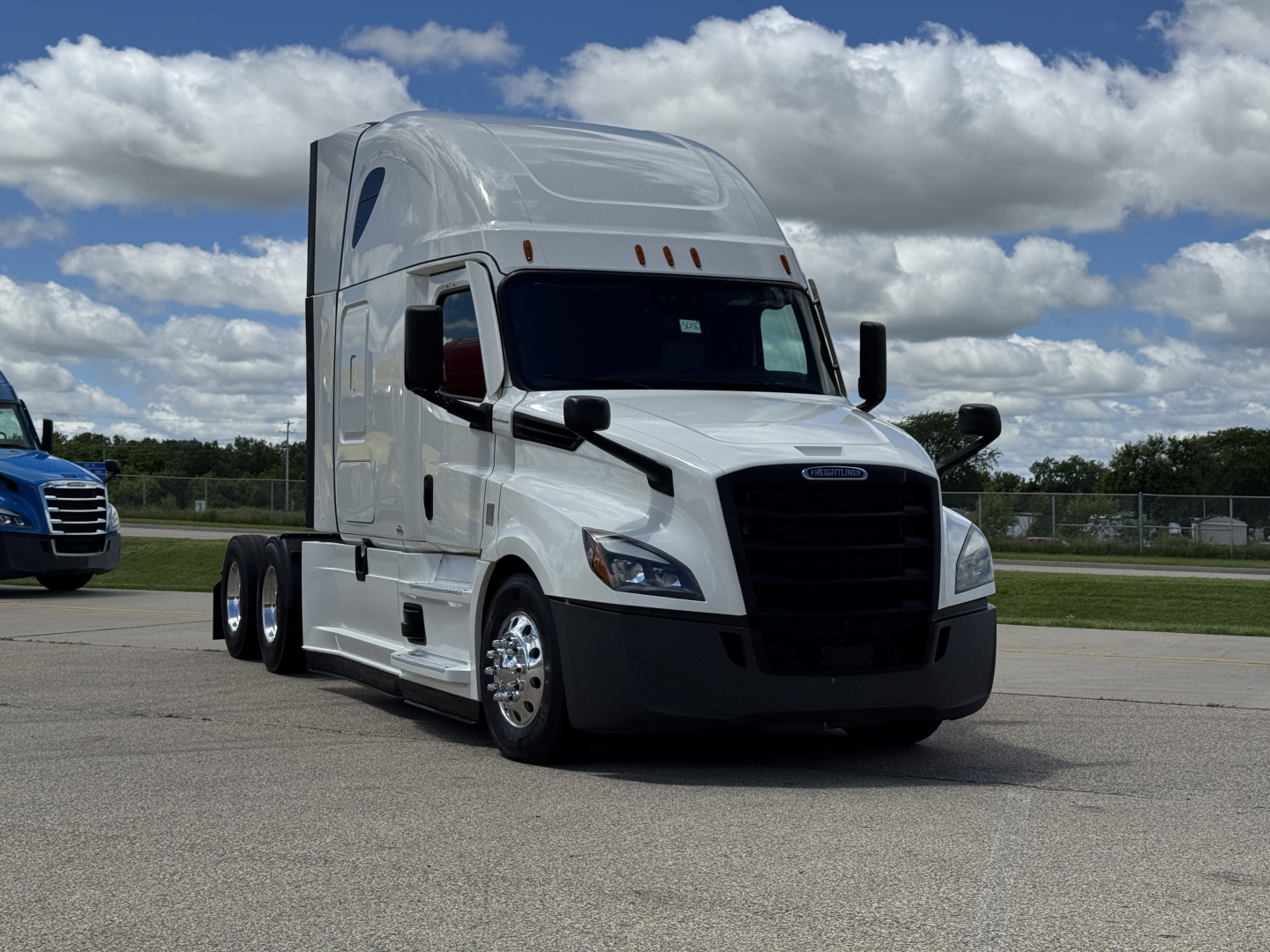 Truck cab in view showing Freightliner Cascadia 126 semi-truck with sleeper, white exterior, black grille, side mirrors, and aerodynamic design.