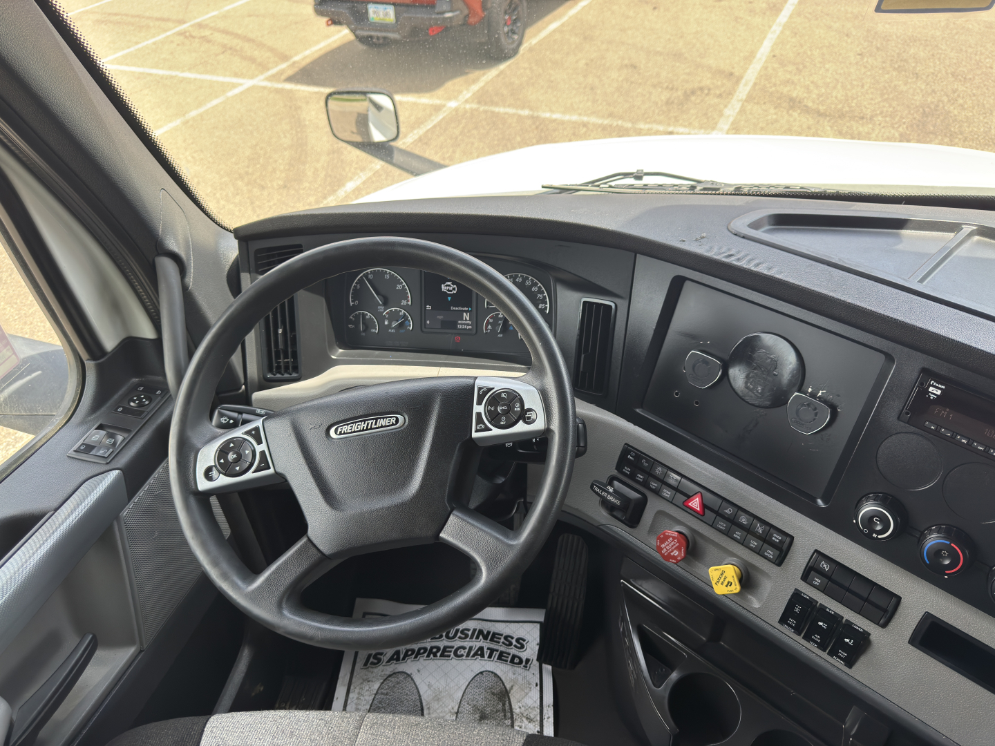 Cab interior of a Freightliner Cascadia with steering wheel, dashboard gauges, and control panel visible.