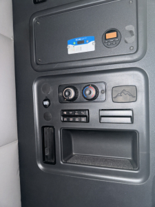 Dashboard area of a 2021 Freightliner Cascadia showing control gauges and a small digital display, with a blue card sticker and a circular device on the panel.