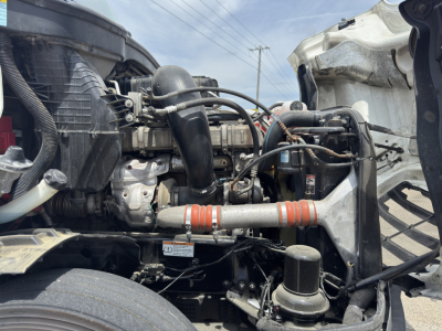 Truck engine bay showing turbocharger, intercooler piping, hoses, and coolant reservoir in a Freightliner Cascadia engine compartment.