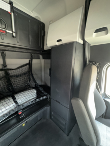 Freightliner Cascadia 126 interior view showing sleeping berth with storage cabinets and seat in cabin.