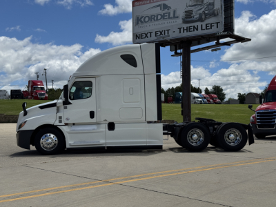 Tractor-trailer in a dealership lot with white Freightliner Cascadia 126 sleeper cab, side view showing chassis and dual rear axles.