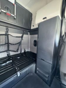 Cab interior of a Freightliner Cascadia sleeper showing storage net and vertical cabinet with panel, side wall, and cargo area.