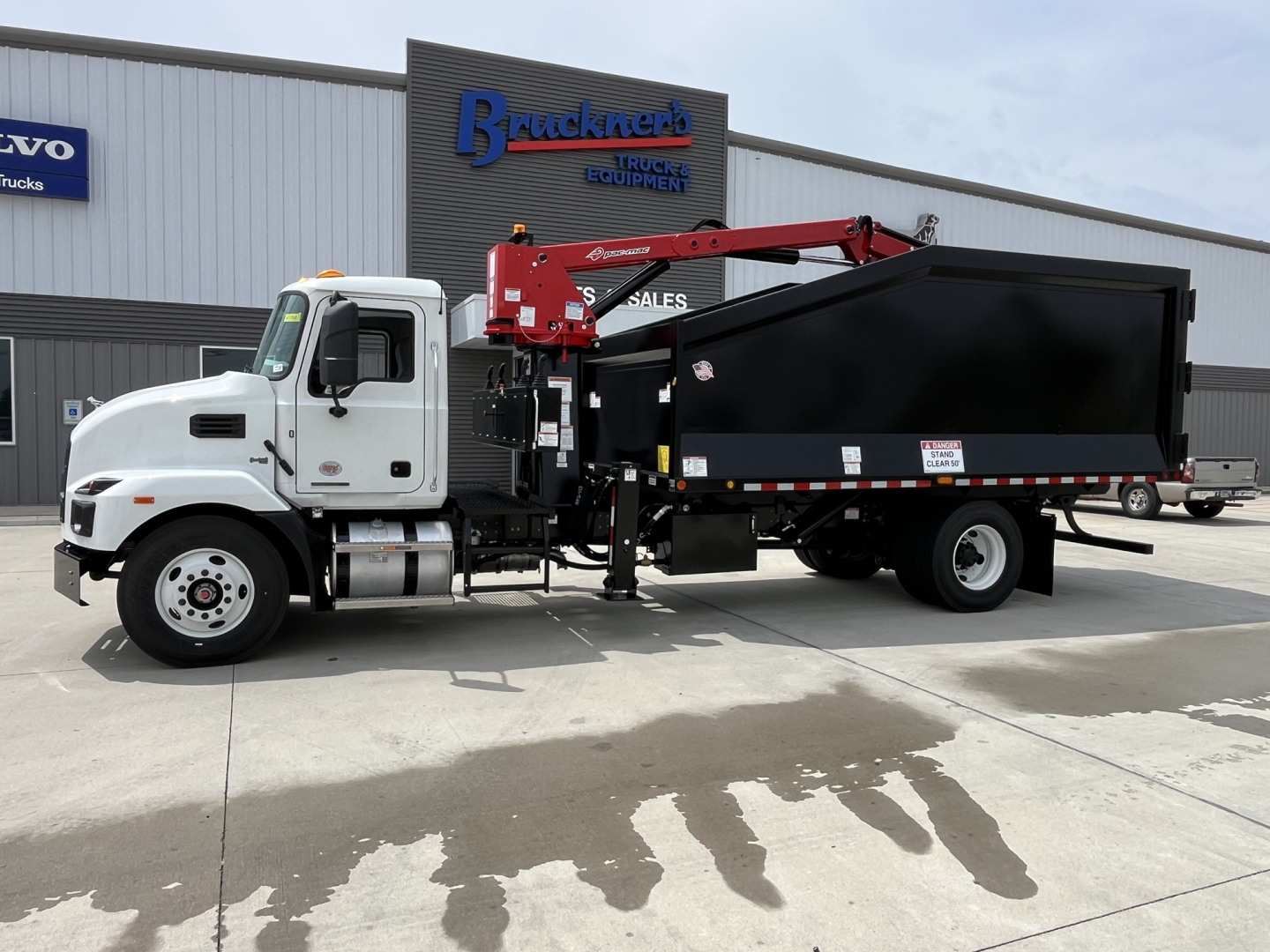 Truck with crane and dump bed, white cab, black dump body, red hydraulic crane mounted on chassis, Mack MD7 model signage not visible.