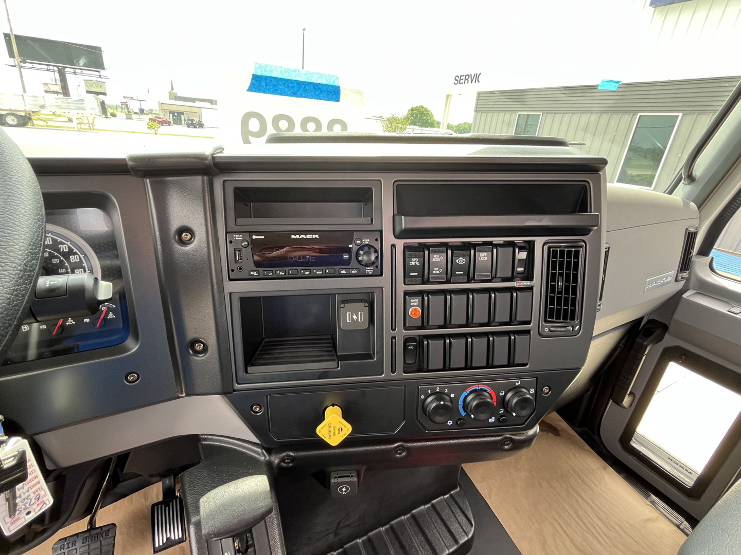 Dashboard and center console of a Mack MD7 truck cab showing radio, control switches, climate controls, and storage pocket.
