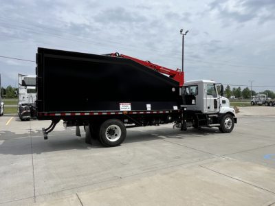 Truck chassis with a large black dump bed and a red crane attached, Mack MD7 in background, side view showing cab and dump body.