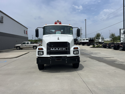 Front view of a white Mack MD7 truck with black grille and bumper, showing the Mack logo; side mirrors; red beacon on roof; other trucks in background.