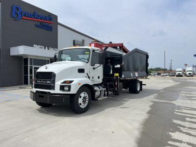 Mack MD7 truck with a grapple/dump body in a dealership lot showing white cab and black bed.