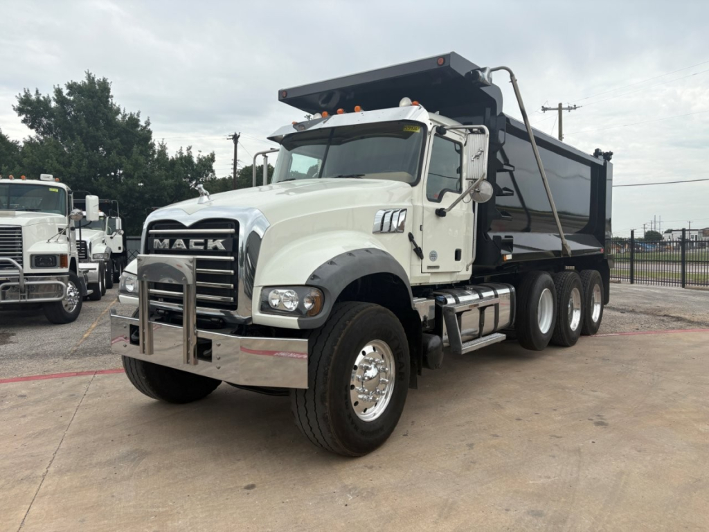 Dump truck showing Mack grille with large bumper guard, white cab, black dump body, front-left angle. Visible text: MACK on grille, stock and VIN in listing context not in image.