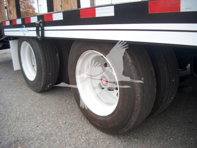 Trailer dual axle tires with white rims and black tire treads under a flatbed trailer, side rails with red/white reflective tape.