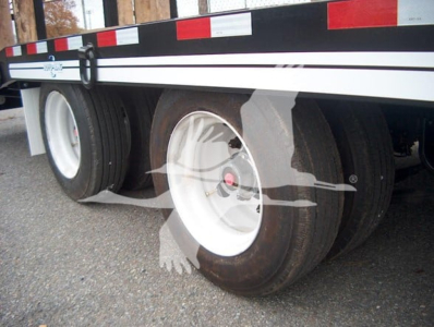Trailer showing dual rear axles with white rims and black tires under a flatbed trailer with reflective red/white tape.