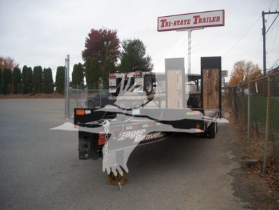 Flatbed trailer in a lot showing Tri-State Trailer sign and logo on the hitch area with a beam and ramps.