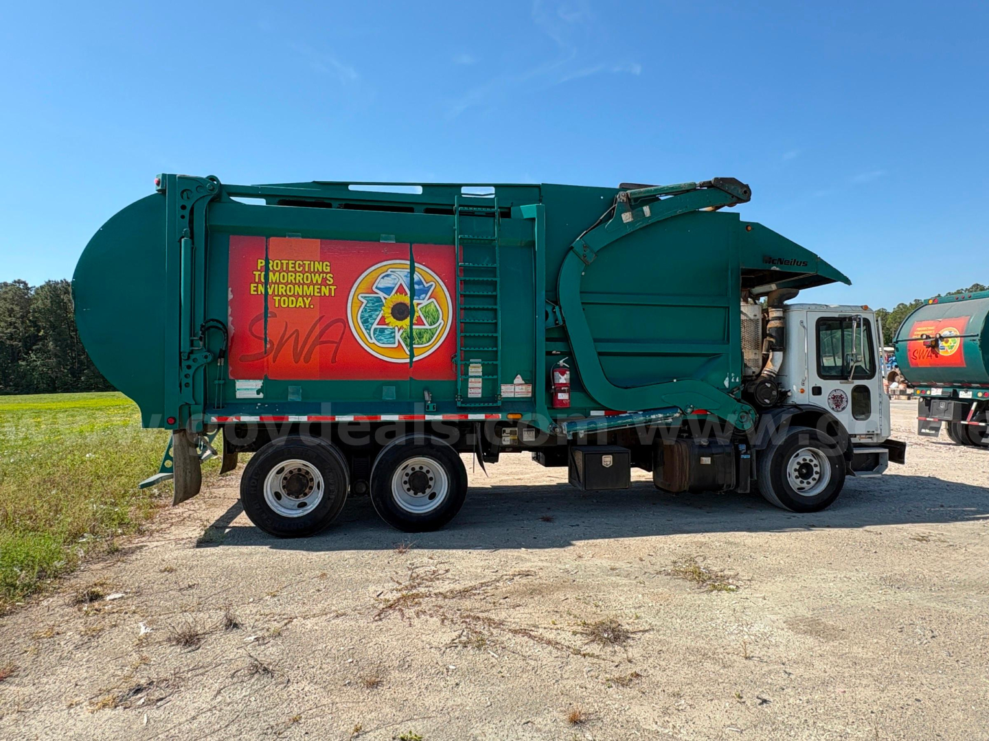 Side view of a green 2012 Mack MRU613 garbage truck with recycling logo on side, white cab, fuel tanks, and wheelset; stock number 1931-204.