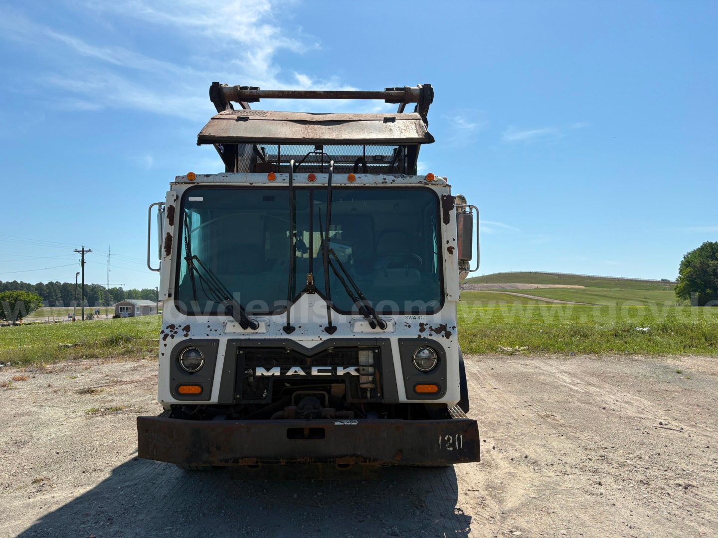 Mack MRU613 front view truck with plow blade, weathered white cab, large windshield and Mack grille.