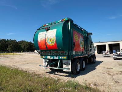 Rear-right view of a green 2012 Mack MRU613 refuse truck with dump body, showing dual rear axles and bumper stickers.