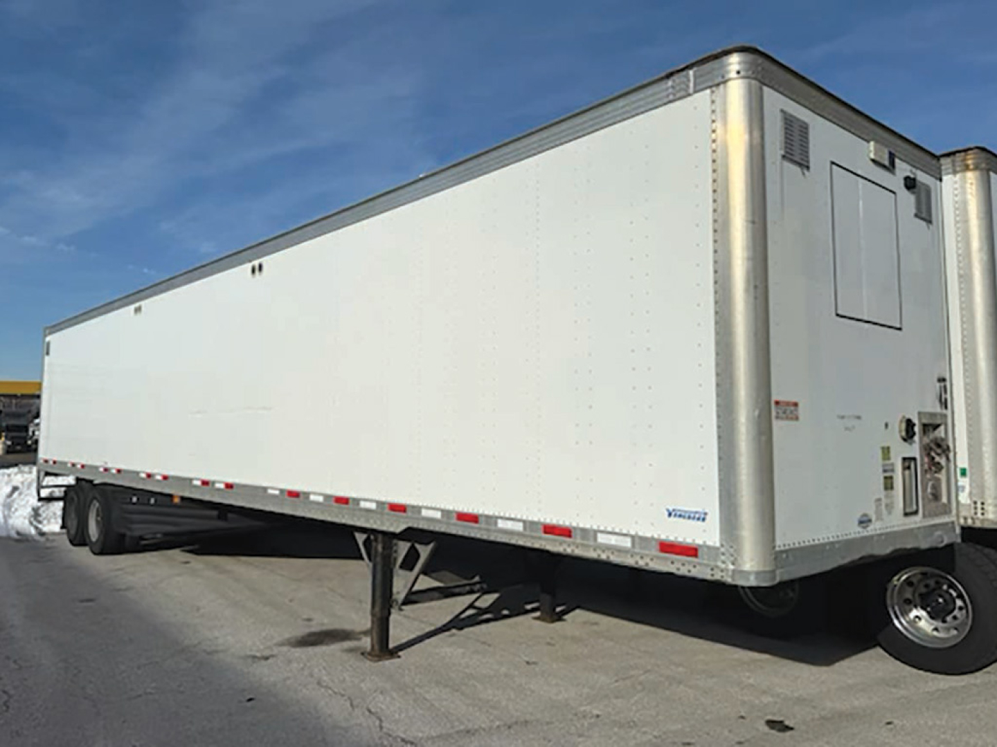 Trailer side view showing aluminum Vanguard van trailer with landing gear down and wheel on front corner.