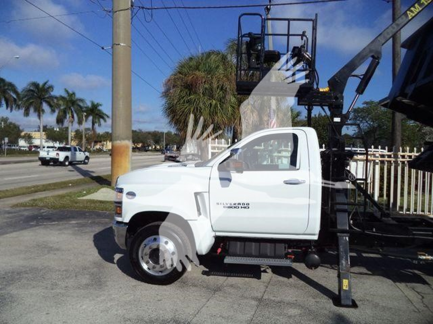 Side view of a white 2023 Chevrolet Silverado 6500HD truck with a mounted aerial device and hydraulic boom in a dealership lot.