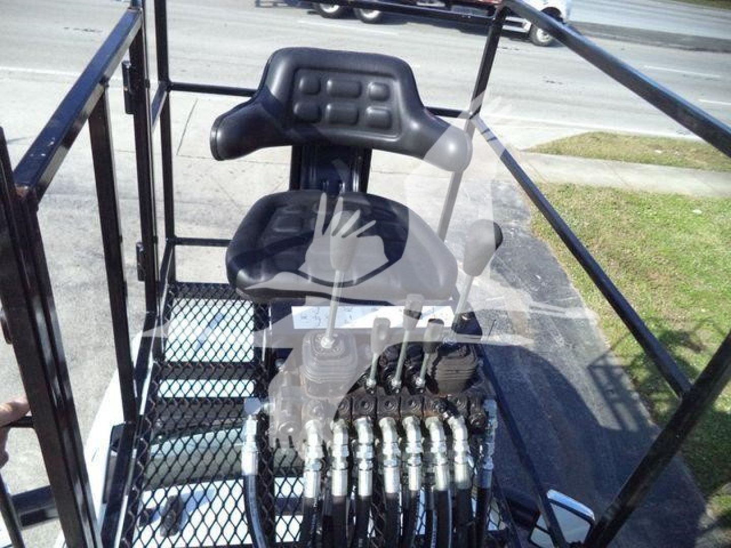 Seat and control levers in open truck bed with hydraulic controls and ladder-style frame.