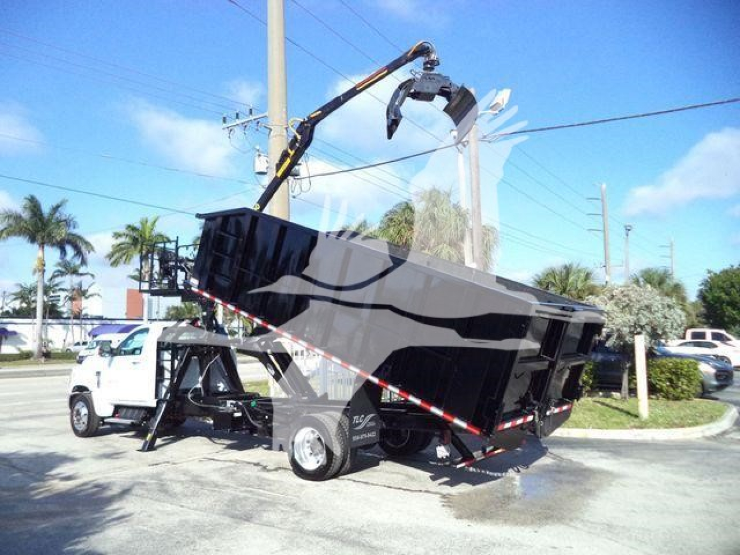 Truck-mounted dump bed on a Silverado 6500HD chassis with hydraulic crane, rear Dump body raised, white cab, black bed, in a dealership lot.