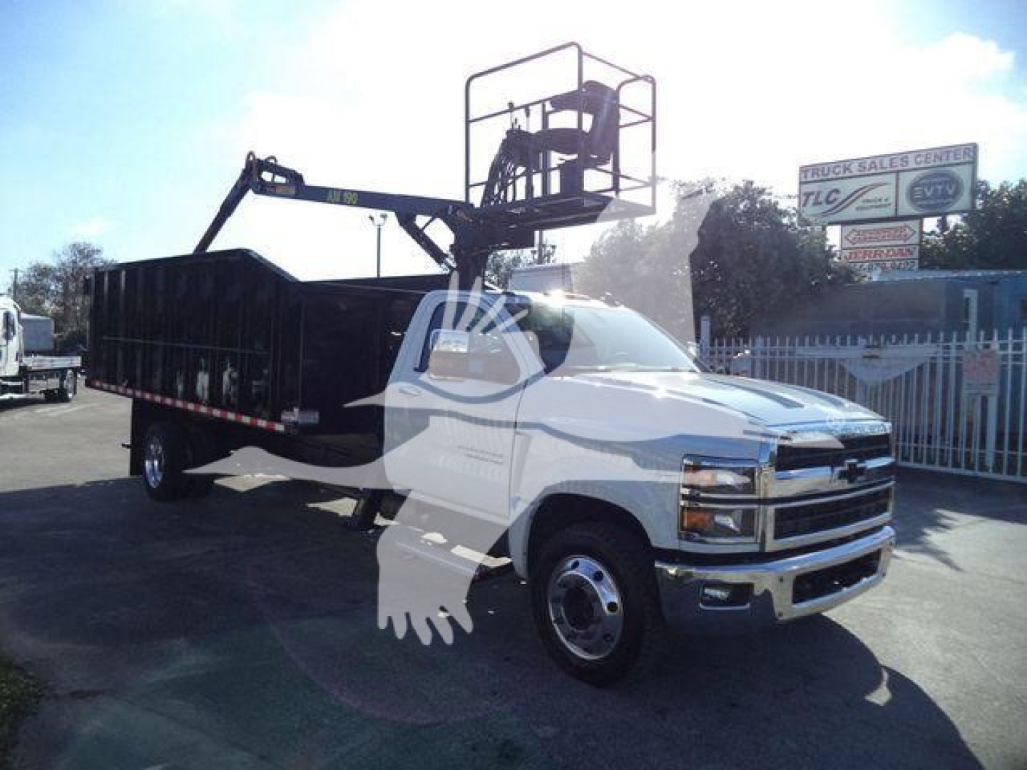 Chevrolet Silverado 6500HD new truck with a bucket lift on a white cab and black dump bed, visible signage in background.