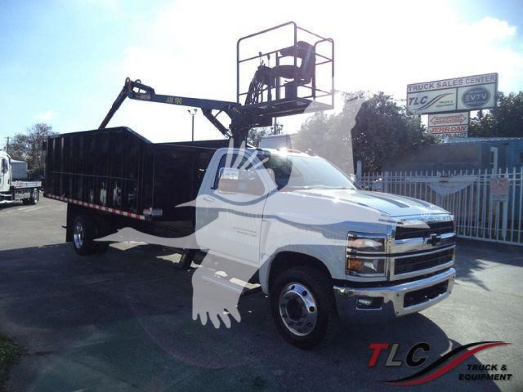 Chevrolet Silverado 6500HD service truck with a rear dumping bed and a mounted aerial lift, white cab, black bed, parked showroom lot.