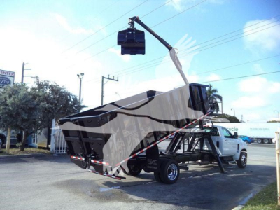 Truck towing a large hoist or crane lift attached to a Silverado 6500HD flatbed, with a lifting bucket mid-air in a parking lot.