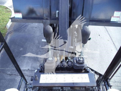 Front interior view of a 2023 Chevrolet Silverado 6500HD cab with two joystick levers and control panel, black spill-proof console, hydraulic controls, and protective cab frame.