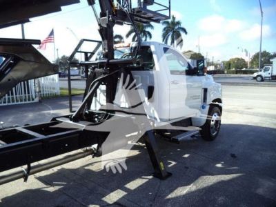Truck cab with lifting equipment and hydraulic arms mounted, white Silverado 6500HD chassis, raised front jack stands visible.