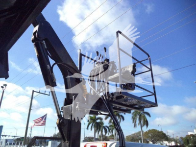 Truck chassis or bucket lift with platform in view, hydraulic arms and metal basket visible against blue sky with palm trees.