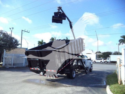 Chevrolet Silverado 6500HD dump truck with a mounted crane in a dealership lot showing a raised bucket near a gate.