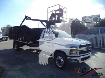 Chevrolet Silverado 6500HD service truck with a rear dumping bed and a mounted aerial lift, white cab, black bed, parked showroom lot.