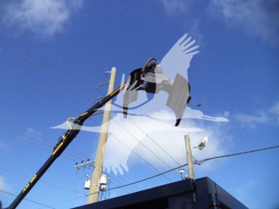 Truck equipment depot image showing a boom crane lifting a device against a blue sky with utility poles and wires.