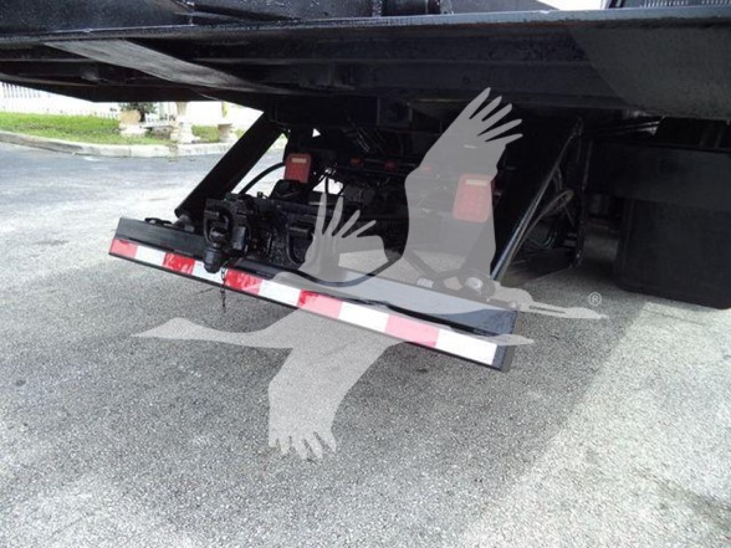 Underneath Freightliner Business Class M2 106 showing tow hitch and hydraulic line components with a drop-down tailgate/rollback mechanism.
