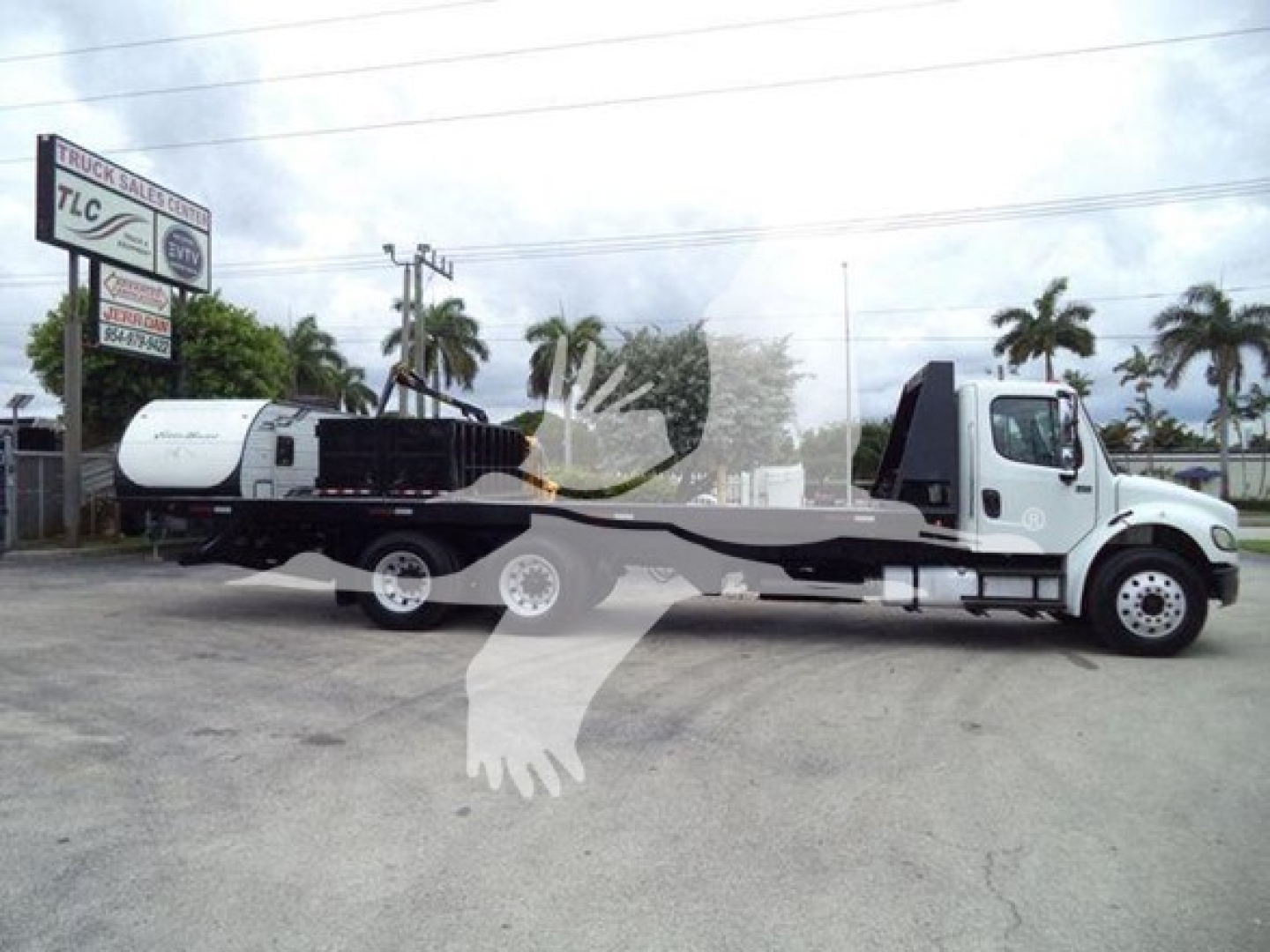 Truck: Freightliner Business Class M2 106 rollback tow truck with a long flatbed, white cab, black flatbed, DOT/brand signage in background.