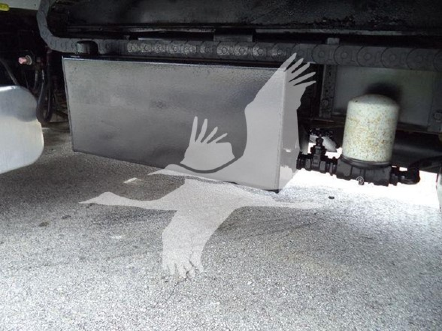 Underbody view of a Freightliner roll-back truck shows a rectangular metal fuel or storage tank and hydraulic lines near the chassis.