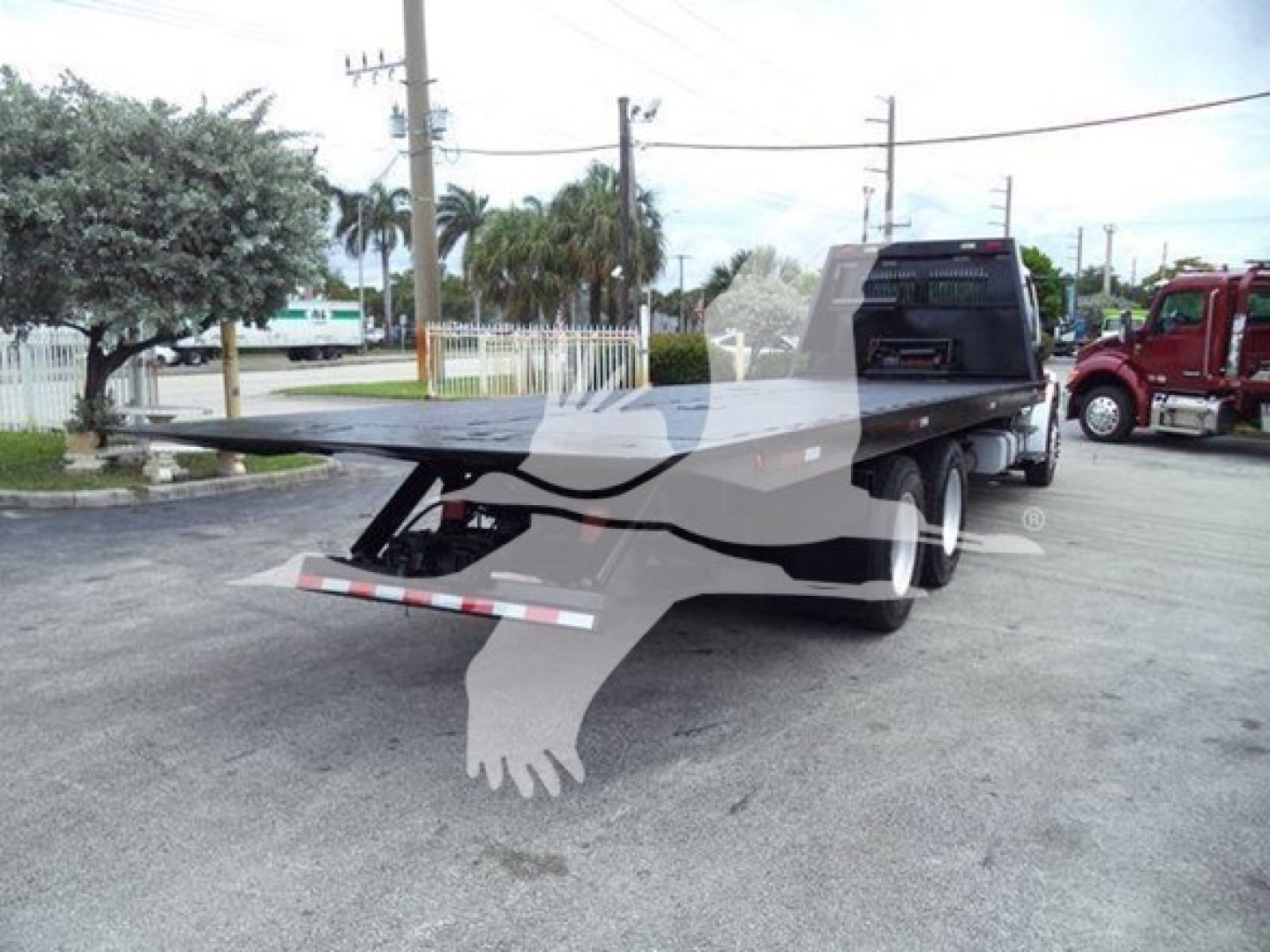 Truck bed of a 2006 Freightliner Business Class M2 106 rollback with flatbed platform and hydraulic winch, rear view showing tires and tail light.