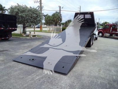 Flatbed wheel-lift tow truck with hydraulic ramp in lowered position and a metal ramp on the ground.
